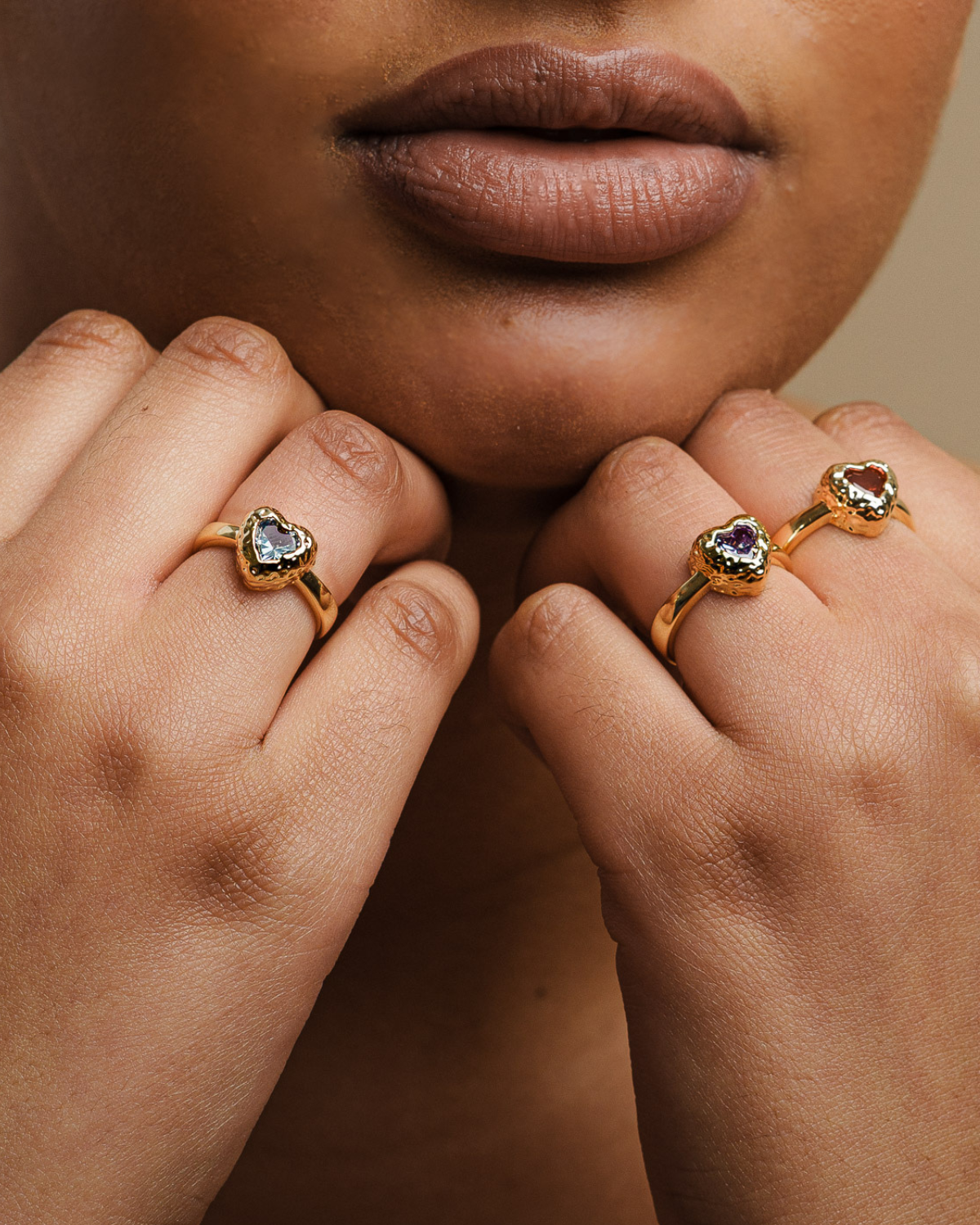 Close-up of hands wearing 18k gold-plated heart rings with colored gemstones
