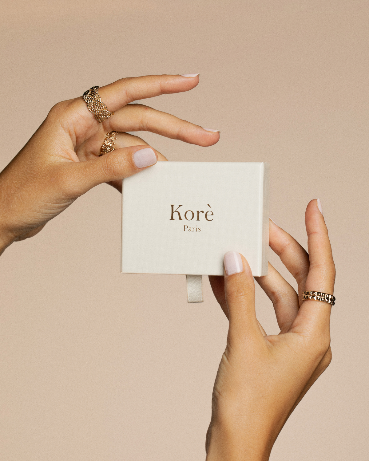Hand holding a white box with 'Korè Paris' branding against a beige background