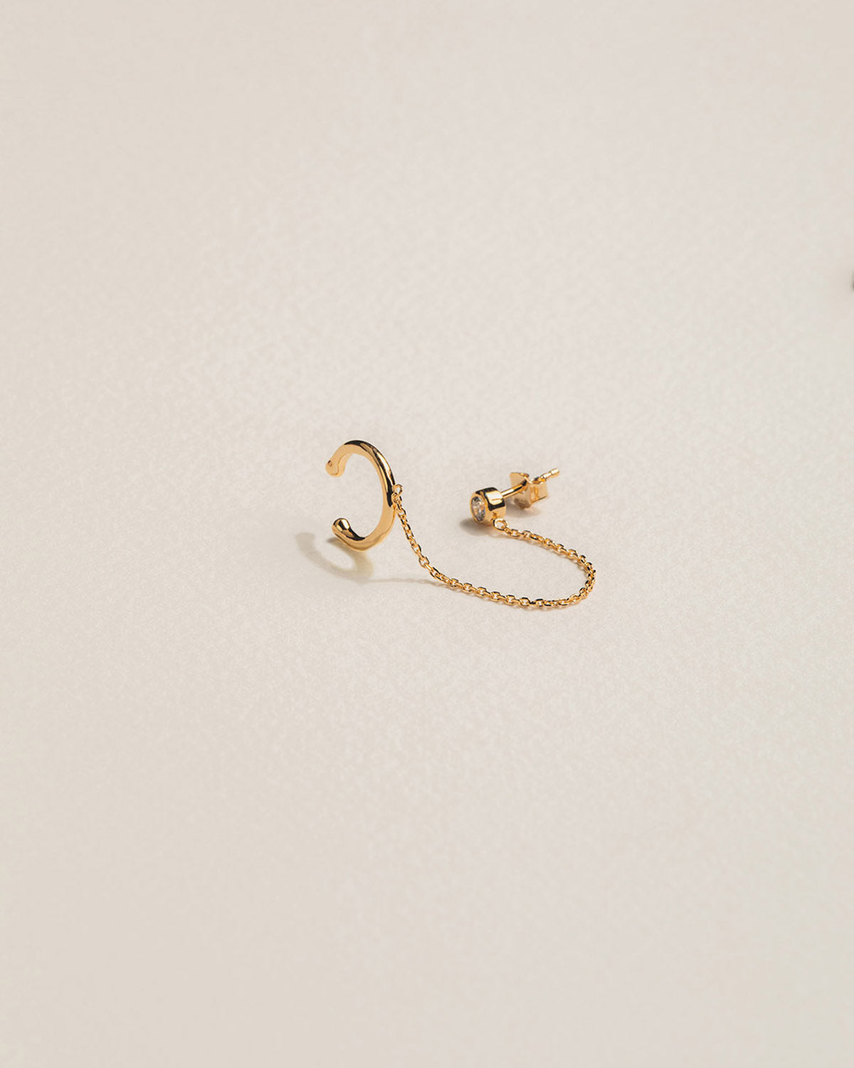 A 18k gold-plated ear cuff with a bezel-set zircon and an attached chain
