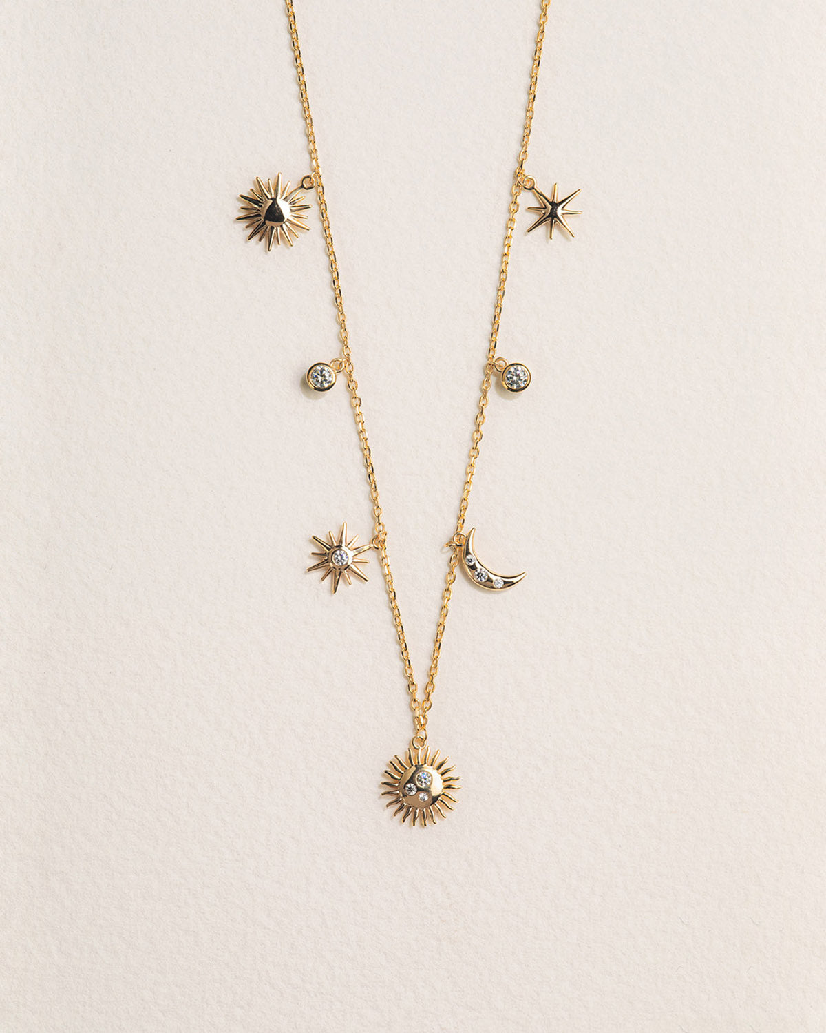 A 18k gold-plated necklace featuring a chain of interlinked sun and moon shapes with dangling stars and a larger central gem.