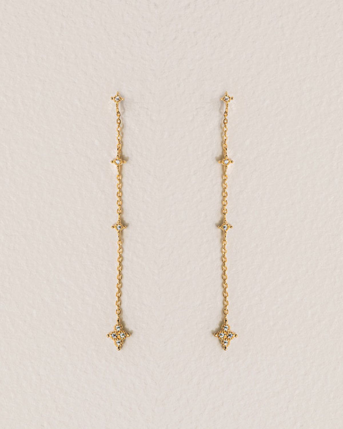 A 18k gold-plated pair of dangling earrings with geometric shaped charms on a delicate chain.