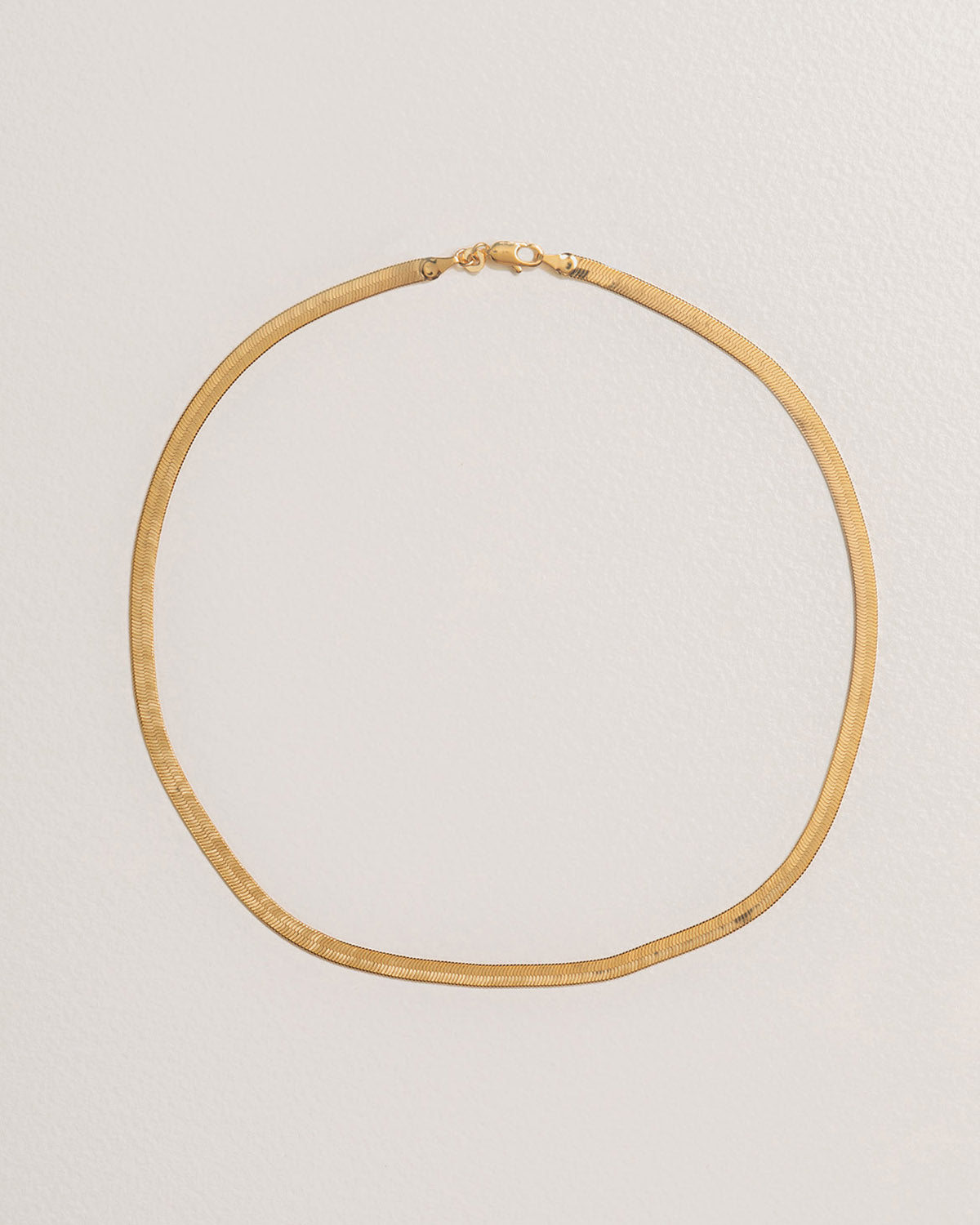 A 18k gold-plated necklace with a flat, smooth serpentine design against a light background.
