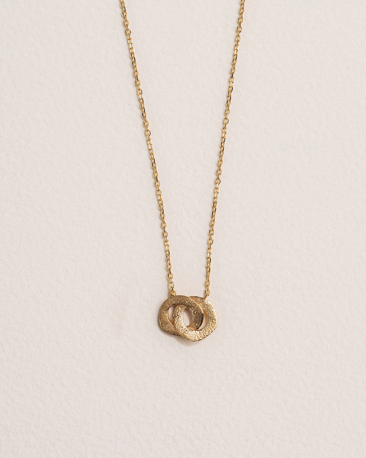 A 18k gold-plated necklace featuring a pendant with two textured intertwined circles.