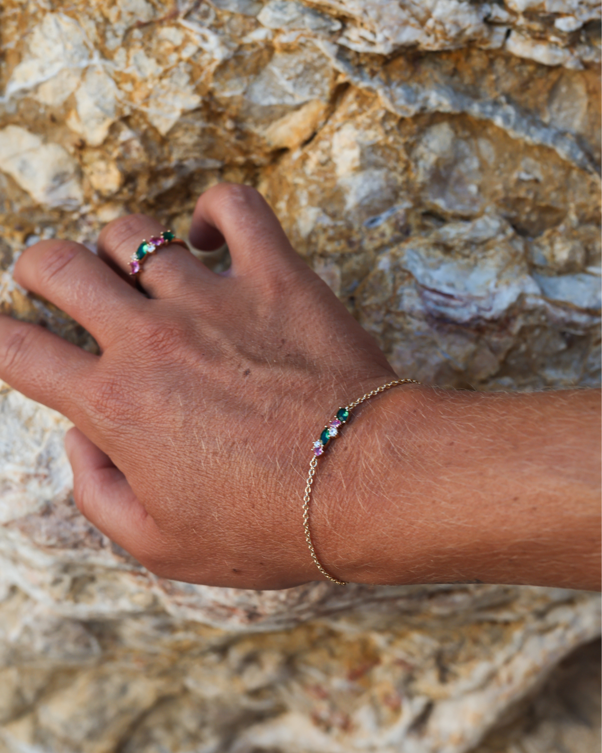 Hand wearing a bracelet and ring with colorful beads against a stone background
