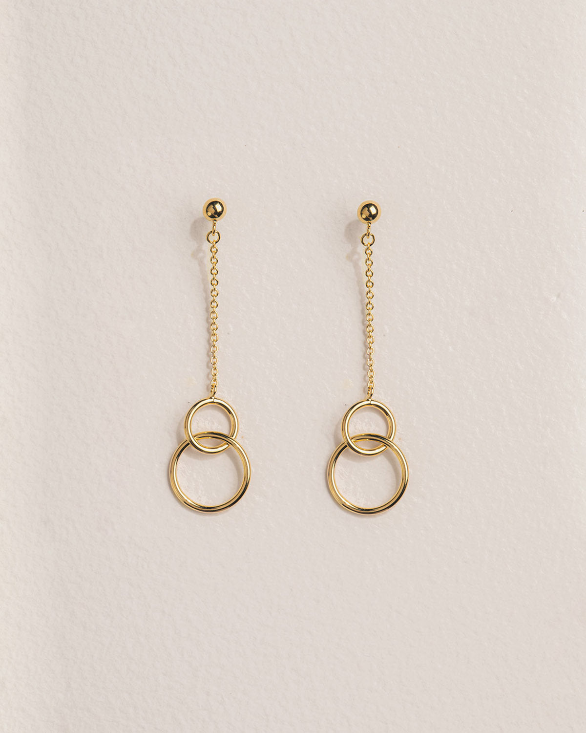 A 18k gold-plated pair of dangling earrings with two intertwined rings in gold color, suspended from a gold chain.