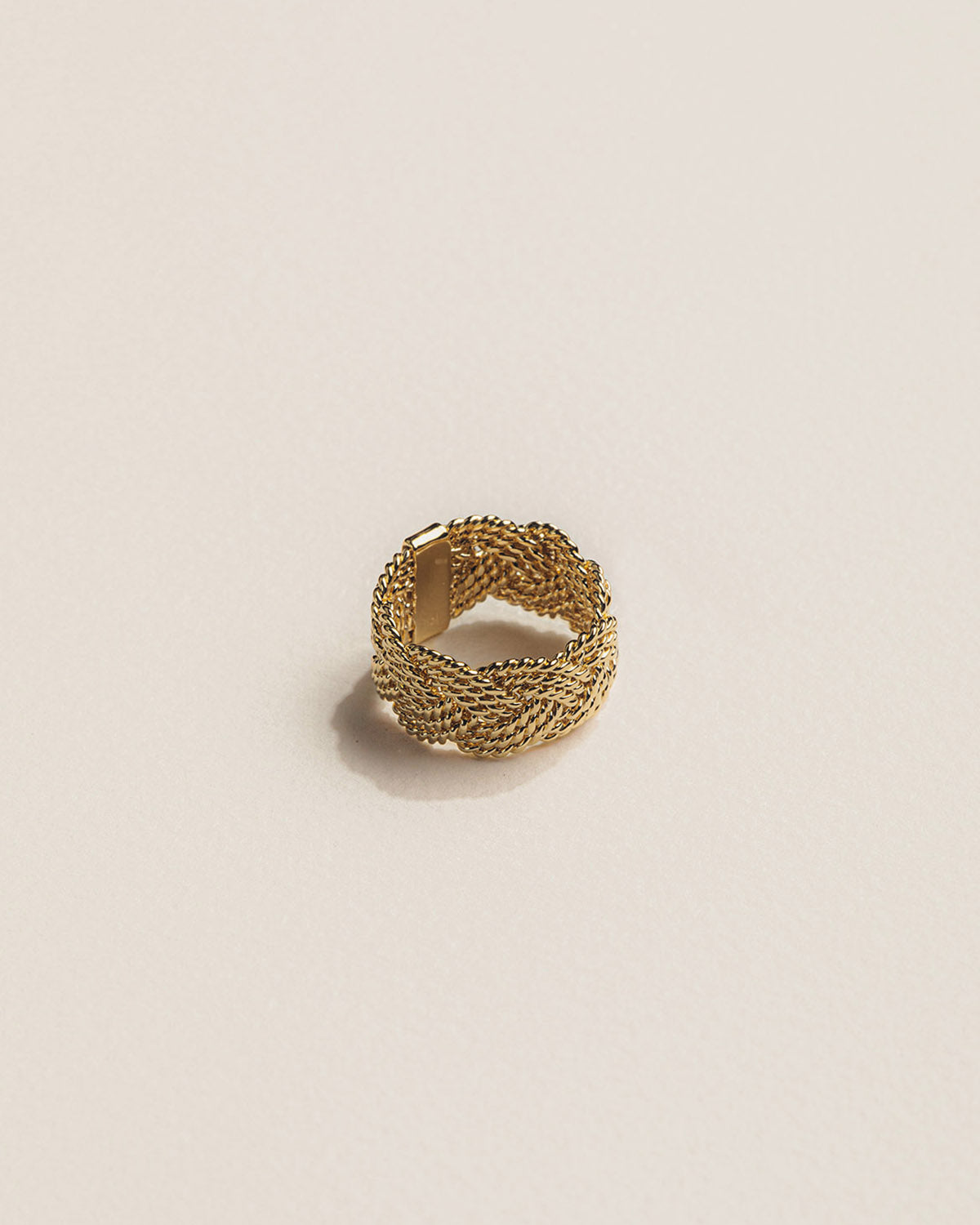 A 18k gold-plated braided ring with intertwined golden links on a textured surface.
